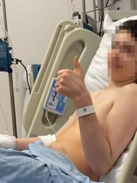menino deitado em cama de hospital após cirurgia fazendo sinal positivo com o dedo