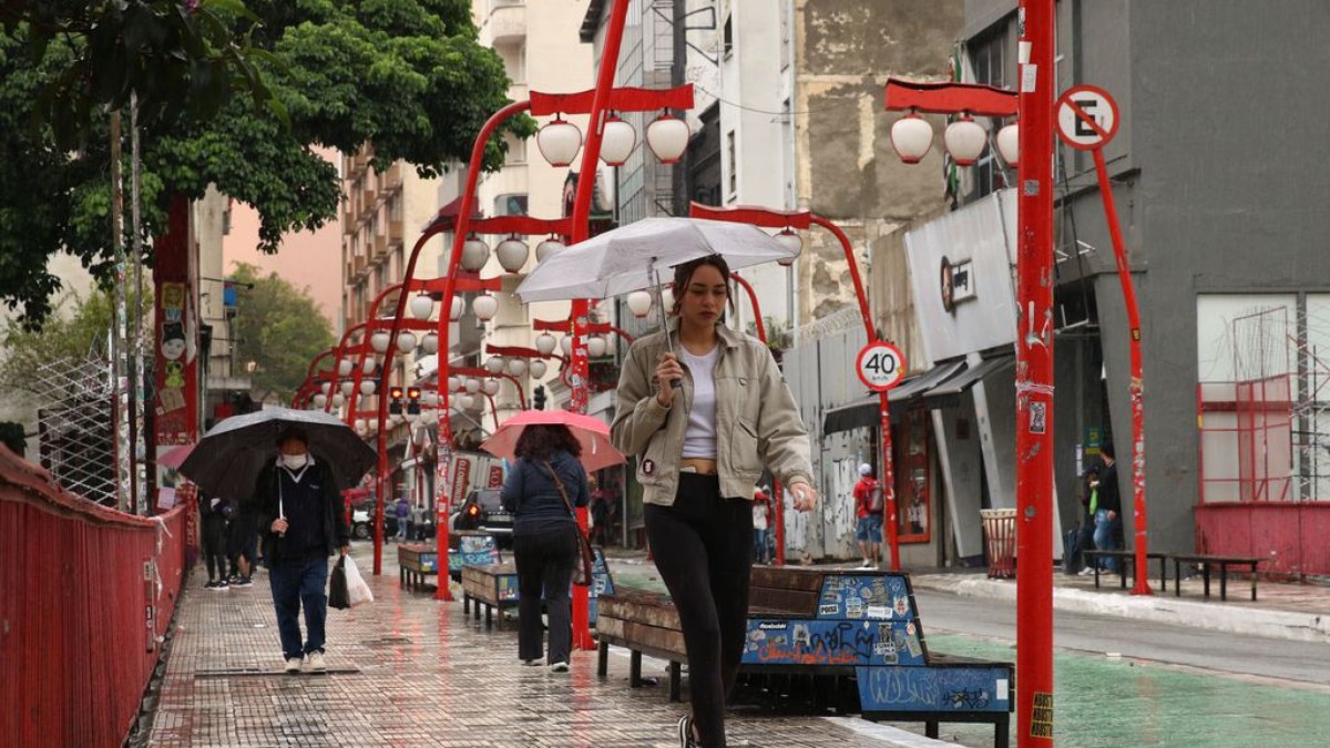 Pedestres se protegem da chuva no bairro da Liberdade durante frente fria na capital