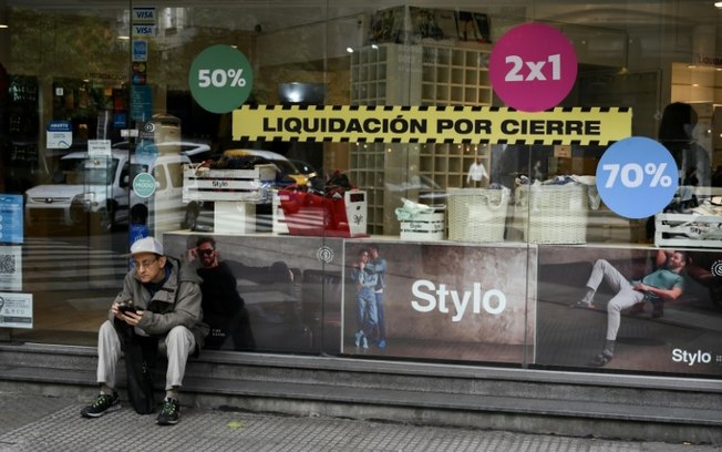 Um homem sentado em frente a uma loja que está fechando as portas em Buenos Aires