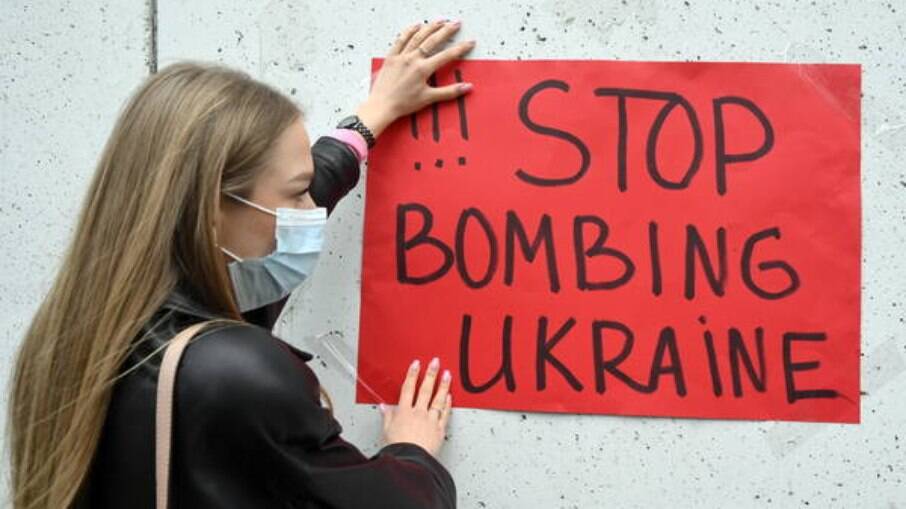 Jovem ucraniana segura cartaz pedindo fim aos bombardeios nem seu país