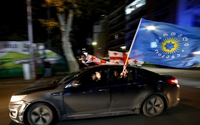 Simpatizantes do partido no poder, Sonho Georgiano, levam bandeiras após pesquisas anunciarem sua vitória nas eleições legislativas, em Tiblissi, em 26 de outubro de 2024