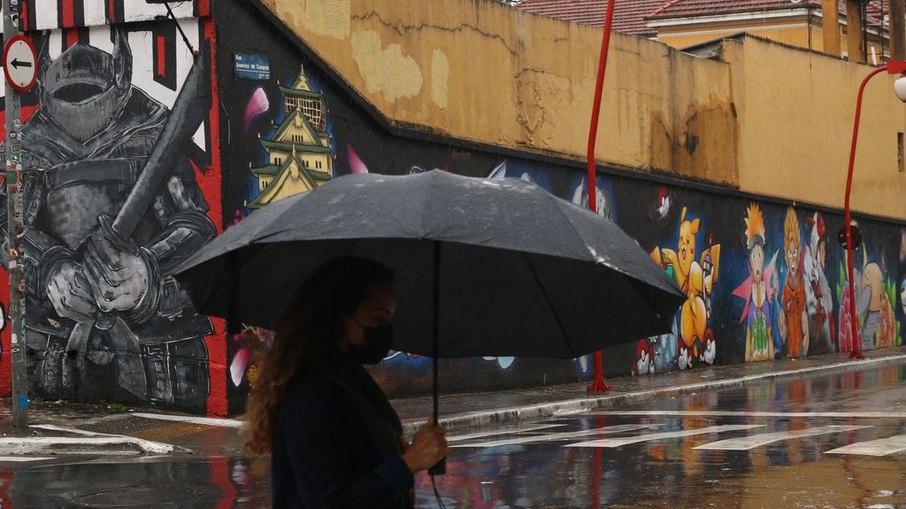 Pedestres se protegem da chuva no bairro da Liberdade durante frente fria na capital