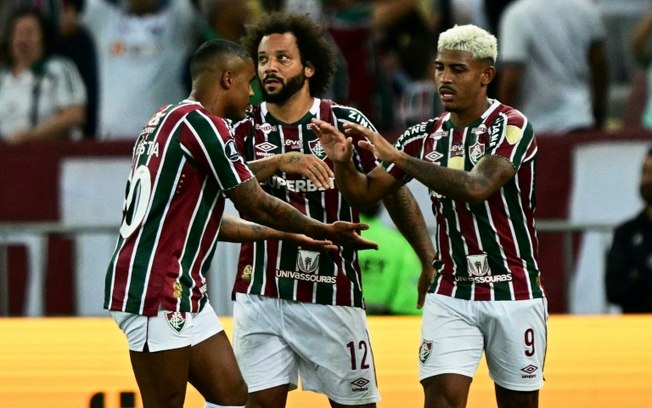 O atacante do Fluminense John Kennedy (dir.) comemora com o meia Douglas Costa (esq.) e o lateral Marcelo (C) após marcar o 3º gol de seu time na vitória sobre o Alianza Lima do Peru no Maracanã, no Rio de Janeiro, em 29 de maio de 2024.