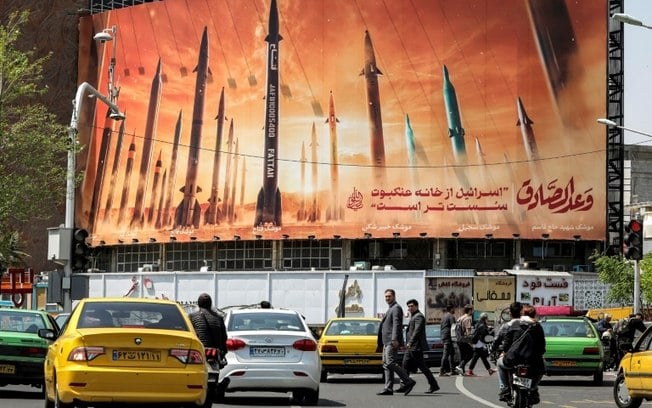 Foto mostra o trânsito em Teerã em 15 de abril diante de cartaz que exibe mísseis balísticos