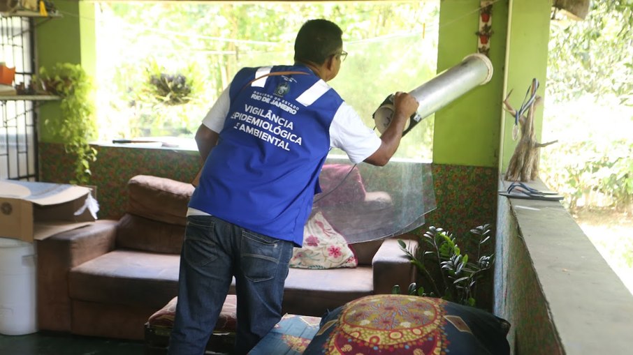 Agente de saúde realiza vistoria preventiva em quintal residencial para identificar e eliminar focos do mosquito Aedes aegypti.