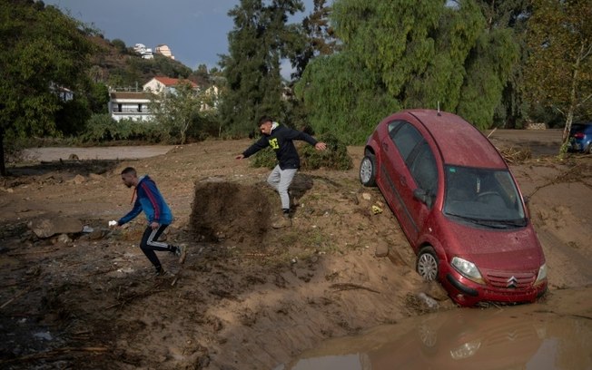 Dois homens correm ao lado de um carro coberto de lama em Álora, perto de Málaga, em 29 de outubro de 2024, depois que fortes chuvas atingiram o sul da Espanha