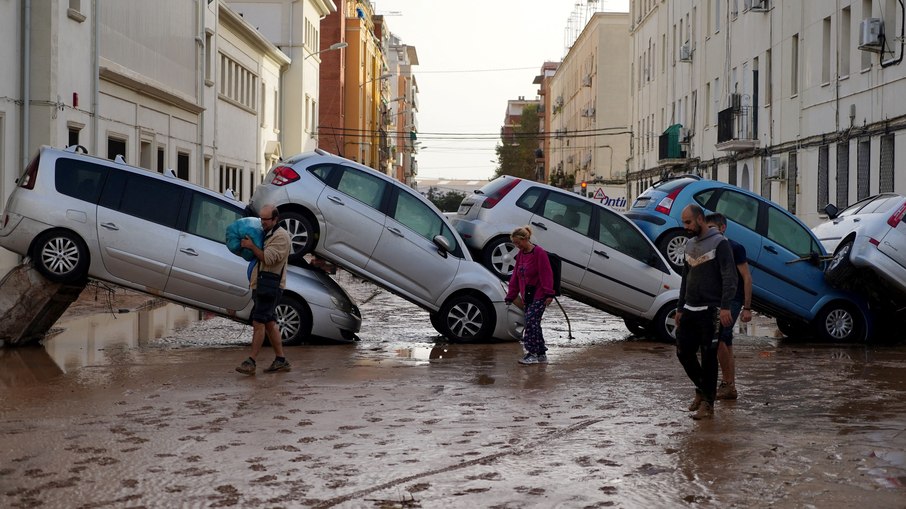 Moradores passam por carros empilhados após inundações mortais no bairro De La Torre, em Valência, a sul de Valência, no leste de Espanha, em 30 de outubro de 2024