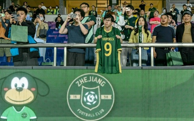 Um torcedor exibe a camisa do jogador gabonês Aaron Boupendza durante a partida da Premier League chinesa entre Zhejiang FC e Meizhou Hakka em Hangzhou, província de Zhejiang, no leste da China, em 16 de abril de 2025. Um torcedor exibe a camisa do jogador gabonês Aaron Boupendza durante a partida da Premier League chinesa entre Zhejiang FC e Meizhou Hakka em Hangzhou, província de Zhejiang, no leste da China, em 16 de abril de 2025.