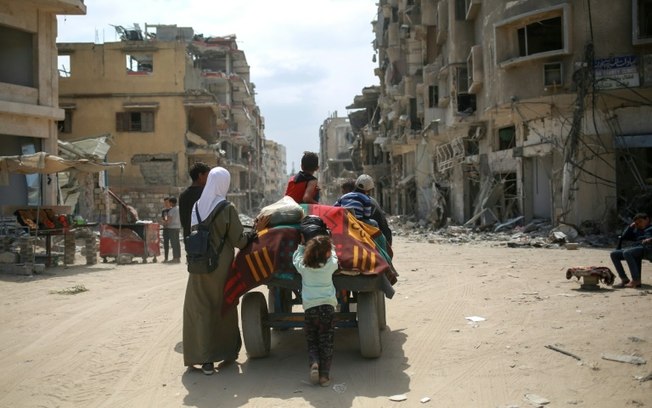 Palestinos carregam seus pertences em uma carroça entre prédios destruídos em Khan Yunis, no sul da Faixa de Gaza, em 2 de maio de 2024