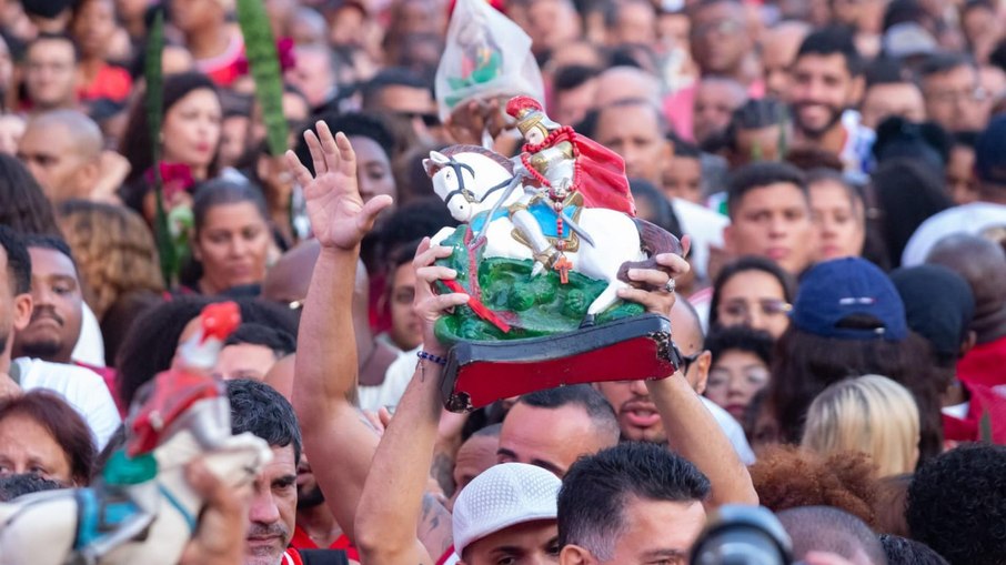  São Jorge montado a cavalo e derrotando o dragão, erguida por um devoto durante uma procissão ou celebração religiosa cheia de fiéis no Brasil