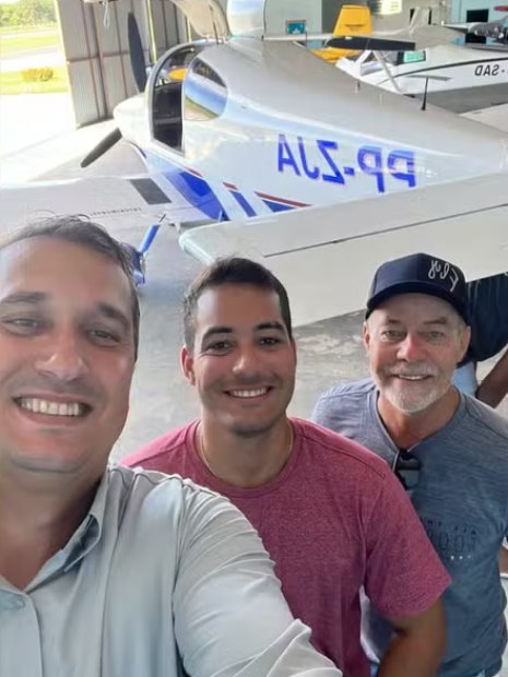 três homens em selfie. eles estão posicionados em frente a um avião de pequeno porte
