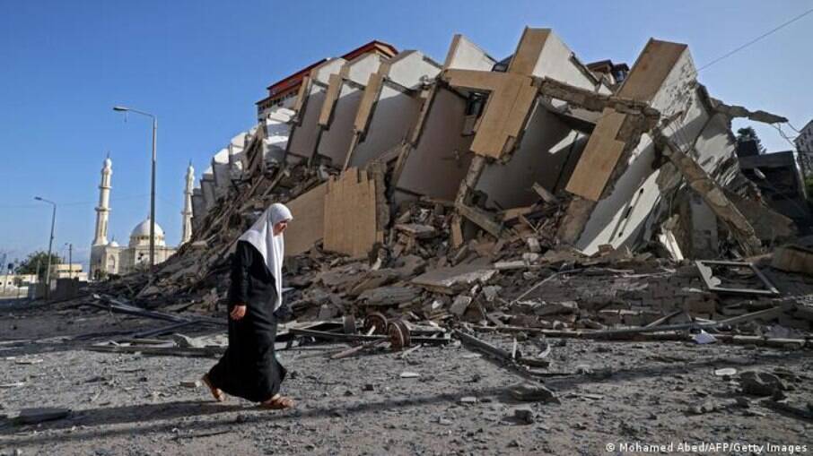 Mulher caminha ao lado dos destroços do prédio de 13 andares derrubado em Gaza por bombardeio Israelense