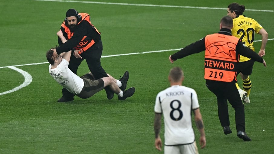 Um invasor de campo é abordado por comissários durante a final da Liga dos Campeões da UEFA entre Borussia Dortmund e Real Madrid, no estádio de Wembley, em Londres, em 1º de junho de 2024. 