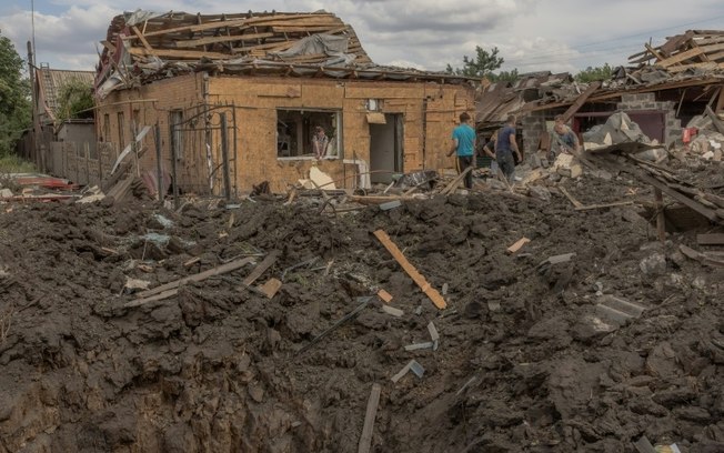 Moradores limpam escombros ao lado de casas fortemente danificadas após bombardeio em Pokrovsk, região leste de Donetsk, em 24 de junho de 2024, em meio à invasão russa na Ucrânia