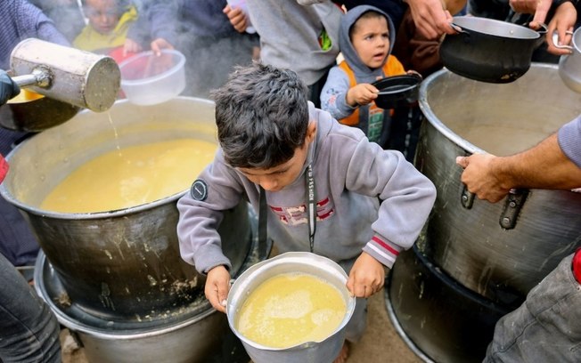 Crianças palestinas recebem prato de lentilhas em um posto de distribuição de comida em Gaza, em  19 de novembro de 2024