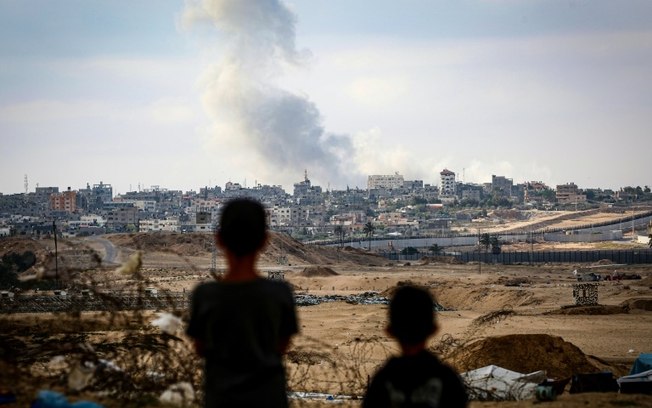 Crianças observam coluna de fumaça durante ataques israelenses no leste de Rafah, sul da Faixa de Gaza, em 13 de maio de 2024