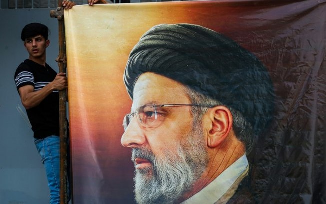 Homens penduram um enorme retrato do falecido presidente do Irã Ebrahim Raisi do lado de fora da embaixada iraniana em Bagdá, em 20 de maio de 2024