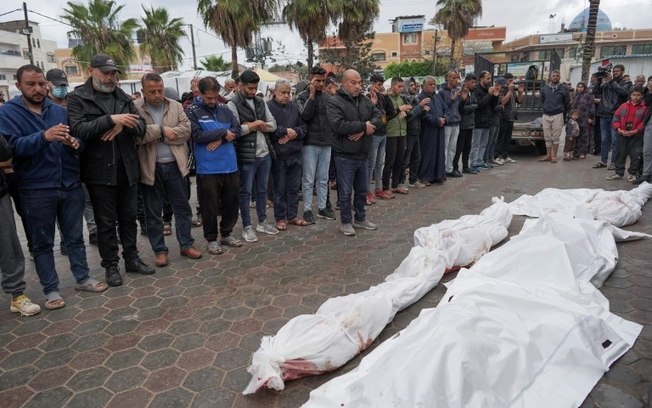 Palestinos rezam ao lado de corpos dos membros de uma mesma família, mortos em um bombardeio israelense no campo de refugiados de Nusseirat, no centro de Gaza, em 10 de abril de 2024