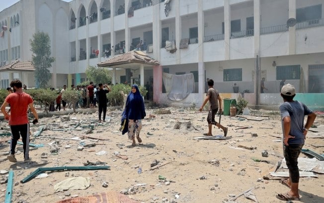 Palestinos caminham entre escombros após bombardeio israelense contra a escola Khadija em Deir al Balah, no centro de Gaza, em 27 de julho de 2024