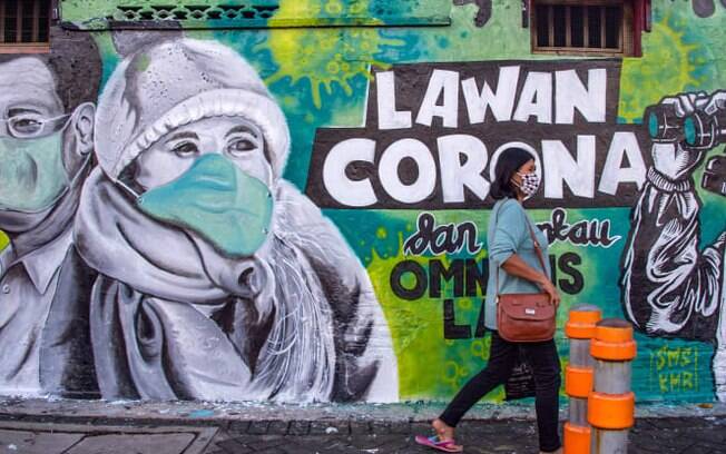 Uma mulher indonésia passa por um mural que convida as pessoas a lutar contra o coronavírus em Surabaya, Java Oriental