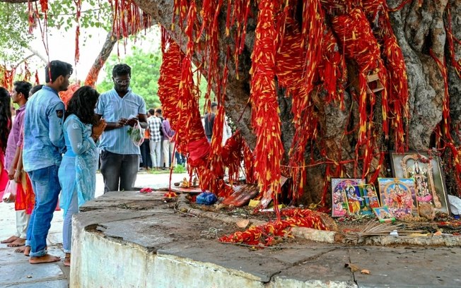 Fiéis hindus rezam depois de pendurar fitas sagradas em uma árvore em um templo dedicado à divindade Balaji, perto de Hyderabad, na Índia, em 24 de julho de 2024