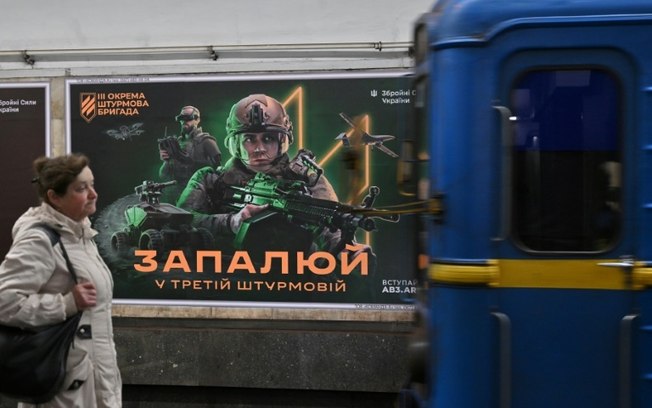 Moradora de Kiev passa por cartaz de recrutamento da 3ª Brigada de Ataque Ucraniana em estação de metrô
