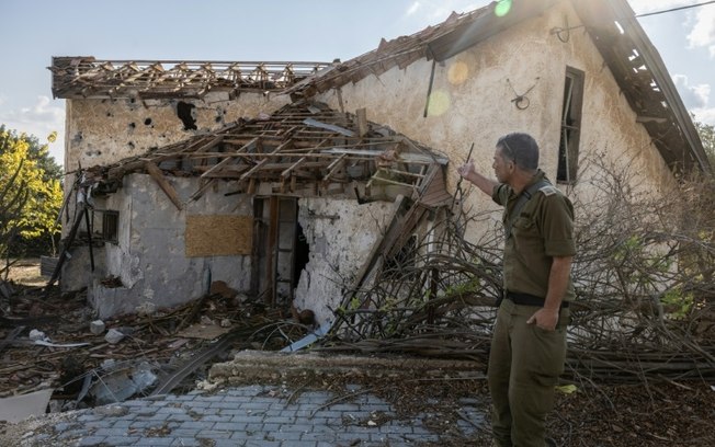 Um soldado israelense aponta para uma casa atingida por foguetes do Hezbollah na cidade deserta de Metula, no norte de Israel, perto da fronteira com o Líbano, em 4 de novembro de 2024