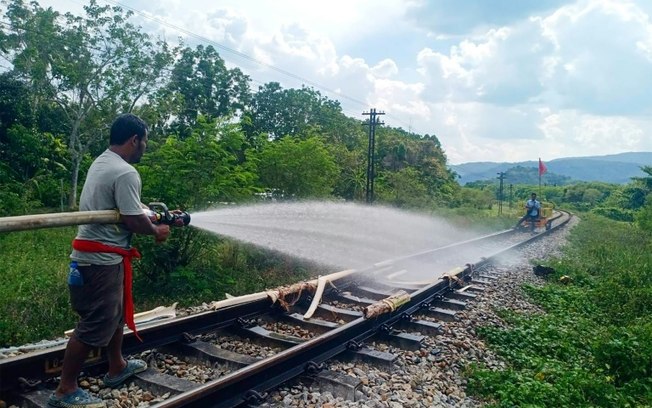 Um trabalhador ferroviário molha os trilhos do trem que derreteram devido ao calor intenso na província de Nakhon Si Thammarat, no sul da Tailândia