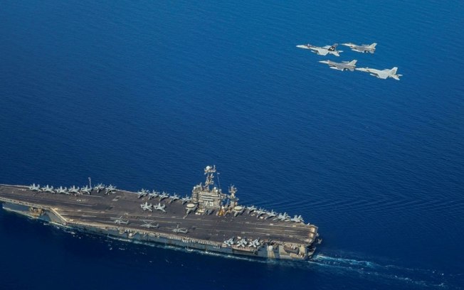 Foto da Marinha dos EUA mostra o USS Harry S Truman com dois jatos F/A-18 e F-16 sobrevoando a embarcação