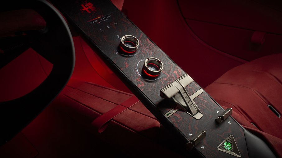 Console central do Cuorerosso reúne comandos giratórios e superfícies digitais, com acabamento que combina elementos metálicos e revestimentos vermelhos.