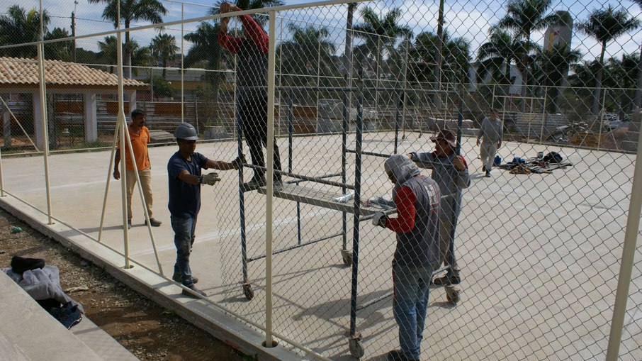 Homens instalam alambrado em quadra de esportes