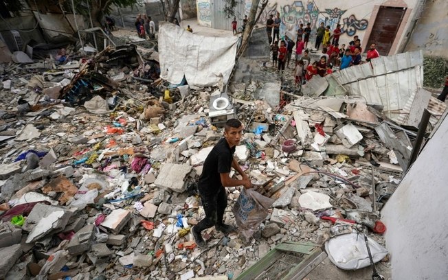 Um menino palestino pega objetos em 30 de maio de 2024 em meio aos escombros de um prédio destruído por um ataque noturno israelense em Nusseirat, no centro da Faixa de Gaza