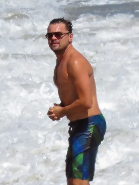 o ator Leonardo DiCaprio em uma praia de bermuda e sem blusa