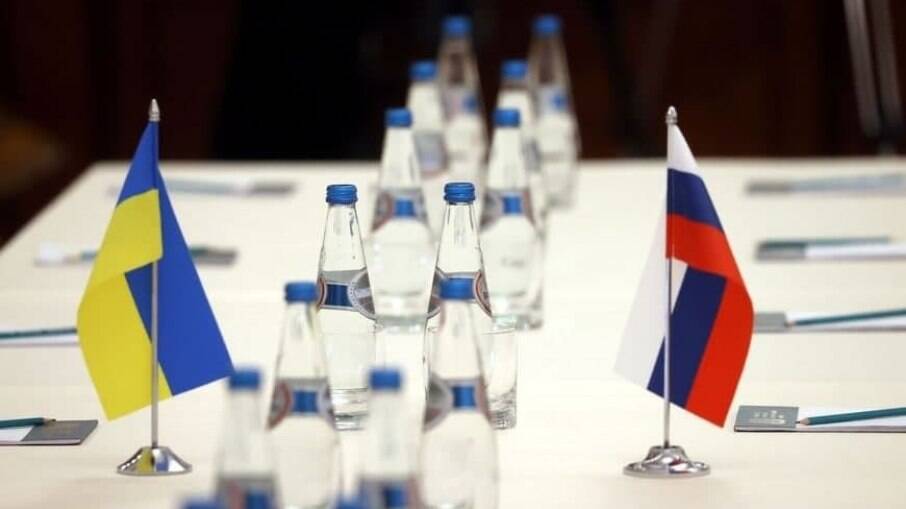 Bandeiras da Rússia e da Ucrânia em uma mesa, em meio a garrafas de água 