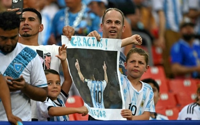 Torcedores argentinos seguram cartaz com a imagem do atacante Lionel Messi antes de amistoso entre Guatemala e Argentina no Commanders Field em Greater Landover, Maryland, no dia 14 de junho de 2024