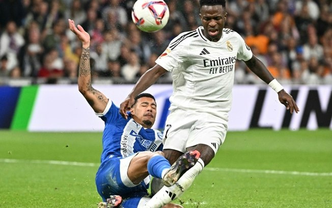 O atacante brasileiro do Real Madrid Vinicius Junior disputa com o meia uruguaio do Alavés Carlos Benavidez durante a partida da liga espanhola no estádio Santiago Bernabéu, em Madri, em 24 de setembro de 2024.