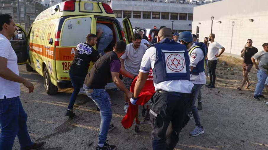 Forças de segurança e médicos israelenses transportam feridos, juntamente com residentes locais, no local onde caiu um ataque do Líbano, na aldeia de Majdal Shams, na zona de Golã anexada a Israel, em 27 de julho de 2024 