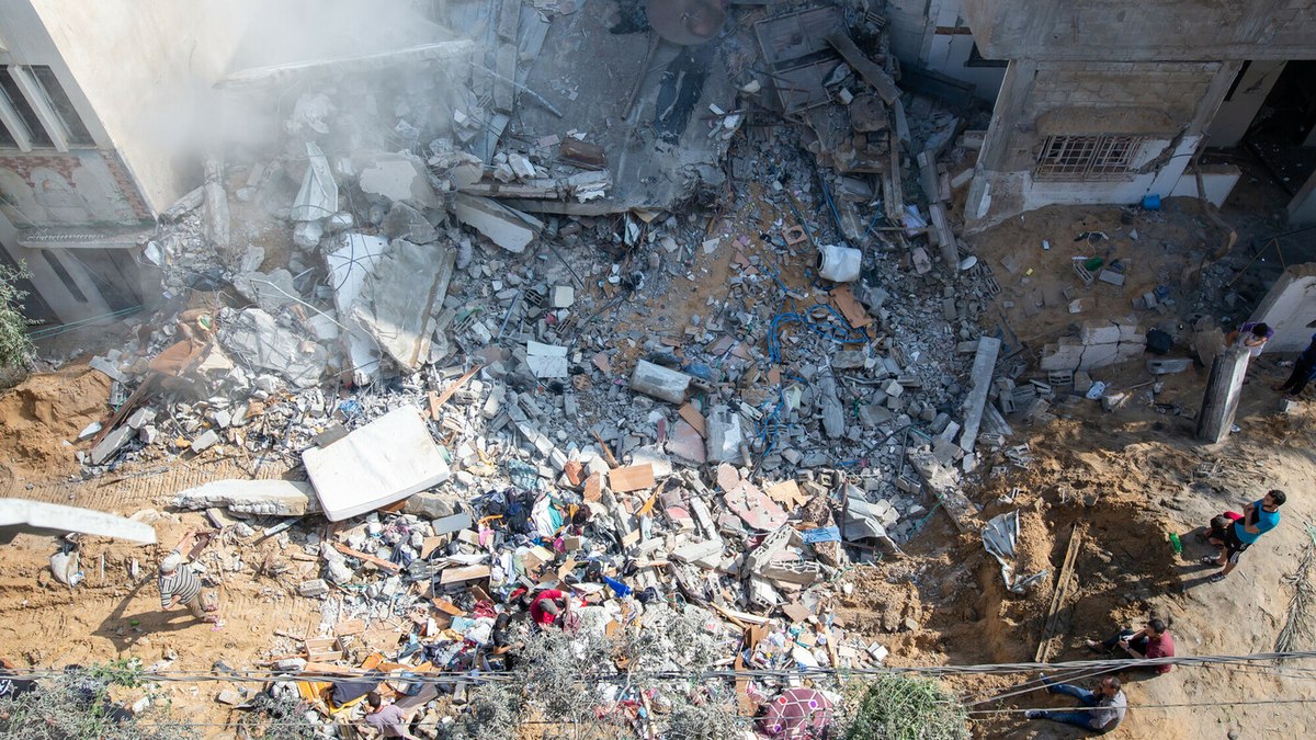 Homens e crianças palestinianos sobre os escombros do seu edifício destruído na área de Al Remal, em Gaza