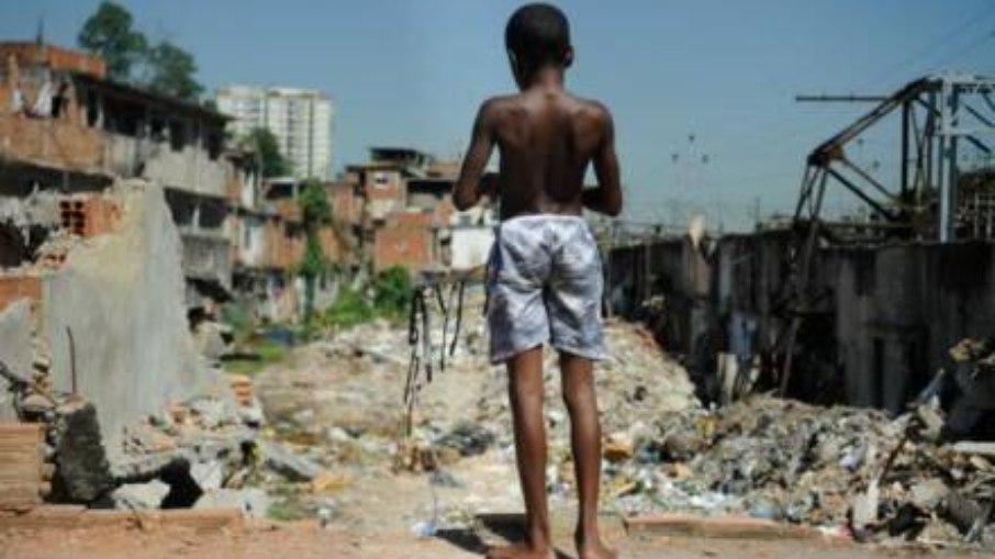Garoto de costas e sem camiseta em meio a entulhos na favela