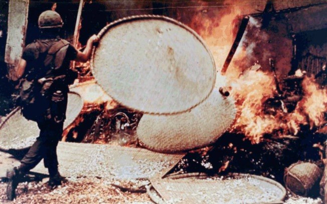 Um oficial alimenta o fogo que ele próprio havia ateado na casa de um morador da aldeia.