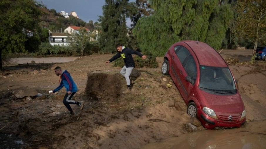 Dois homens correm ao lado de um carro coberto de lama em Álora, perto de Málaga, em 29 de outubro de 2024, depois que fortes chuvas atingiram o sul da Espanha