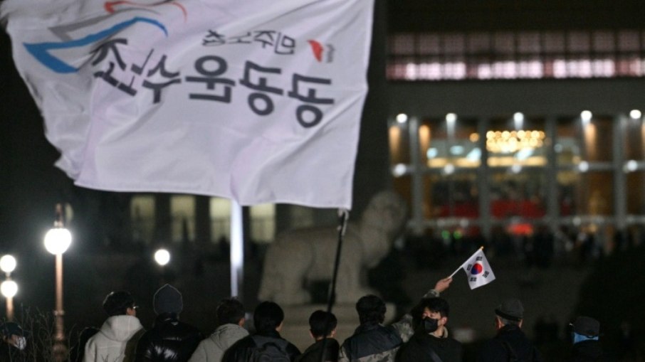 Homem tremula bandeira sul-coreana em frente à Assembleia Nacional em Seul, na Coreia do Sul, em 4 de dezembro de 2024