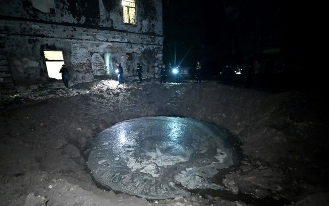 Agentes das forças de segurança inspecionam cratera perto de edifício após ataque com mísseis em Kharkiv, na madrugada de 27 de abril de 2024