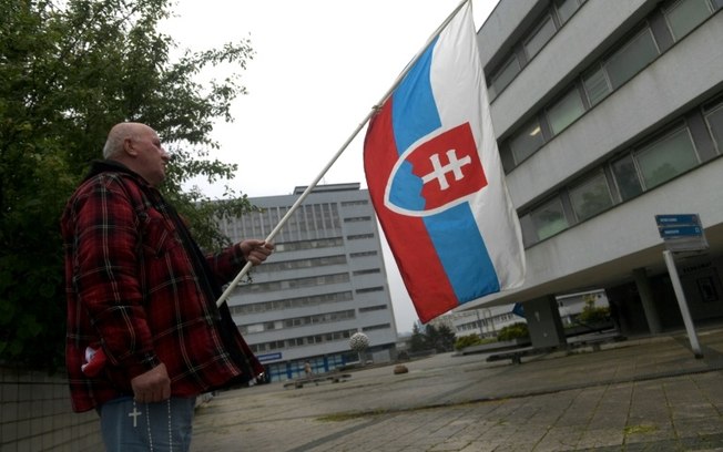 Apoiador agita bandeira eslovaca em frente ao hospital onde está o primeiro-ministro Robert Fico em 17 de meio de 2024 Apoiador agita bandeira eslovaca em frente ao hospital onde está o primeiro-ministro Robert Fico em 17 de meio de 2024