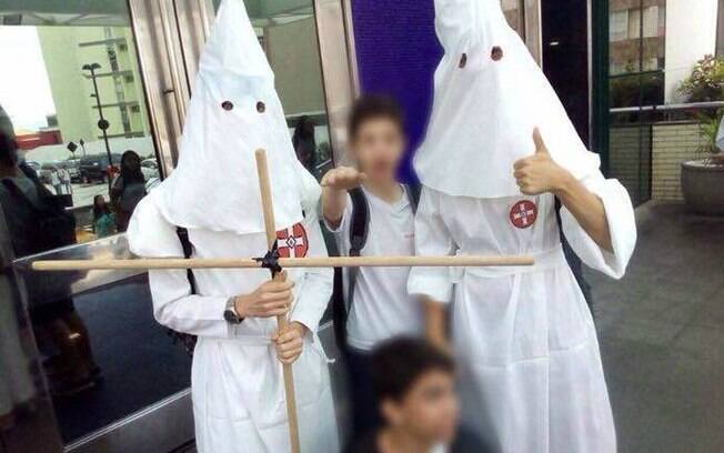 Estudante faz gesto de saudação nazista ao lado de outros dois indivíduos com fantasia da Ku Klux Klan