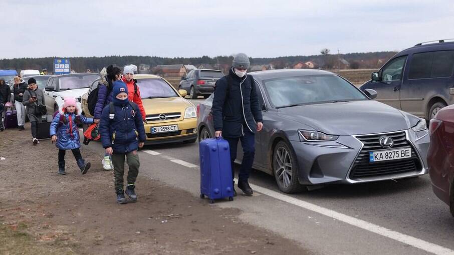 Pessoas que fogem da Ucrânia caminham ao longo de veículos que fazem fila para cruzar a fronteira para a Polônia