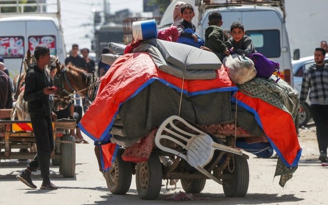 Crianças palestinas sentam-se sobre os pertences de suas famílias enquanto fogem dos combates em Nuseirat, centro de Gaza, 12 de abril de 2024