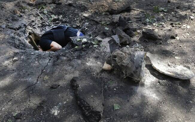 Membro de equipe antibomba inspeciona cratera com os restos de um projétil depois de uma noite de combates em Donetsk, Ucrânia (6/08). Foto: AP