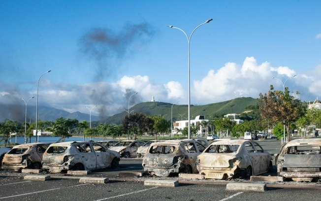 Carros queimados no estacionamento do antigo hospital nos arredores de Numeia em 16 de maio de 2024, durante protestos contra um projeto de lei constitucional que busca ampliar o eleitorado para as próximas eleições na Nova Caledônia