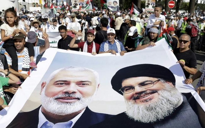 Manifestantes seguram faixa gigante com imagens do líder do movimento palestino Hamas, Islamil Haniyeh (E), e do líder do grupo libanês, Hassan Nasrallah, em uma manifestação em apoio aos palestinos em Rabat, capital do Marrocos, em 6 de outubro de 2024